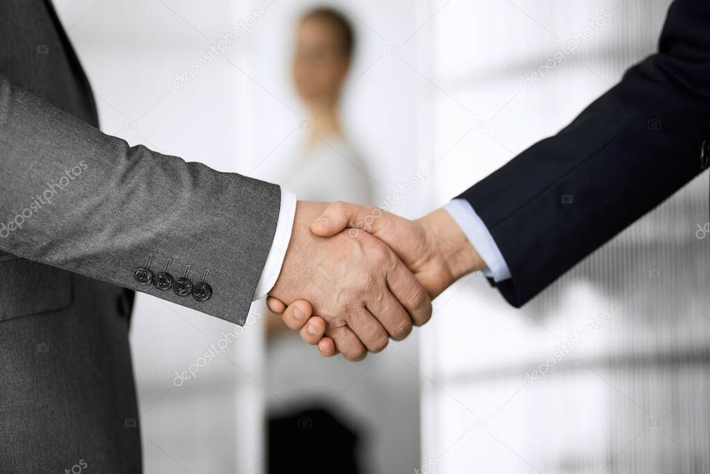 Business people in office suits standing and shaking hands, close-up. Business communication concept. Handshake and marketing