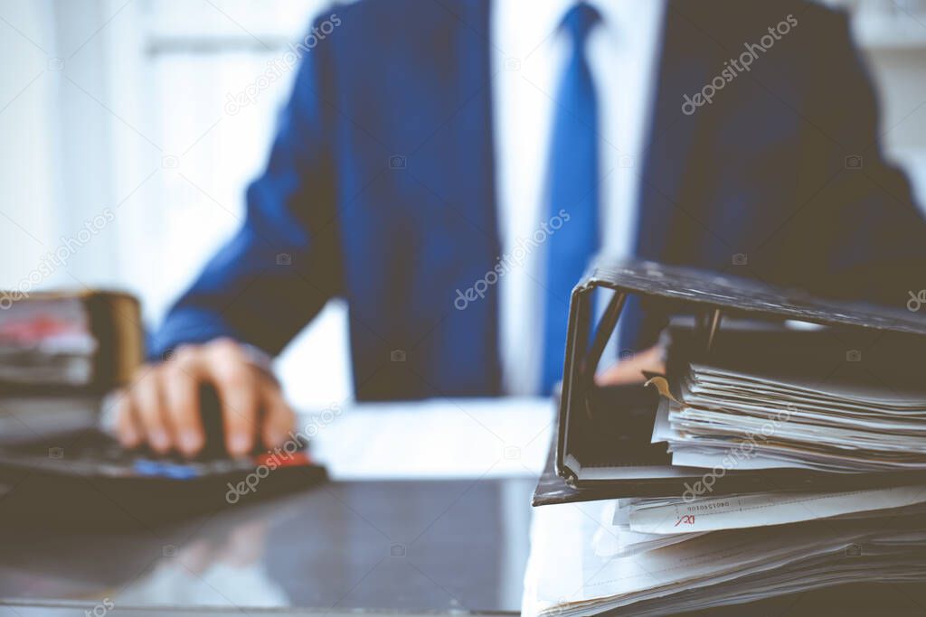 Binders with papers waiting to be processed with businessman or bookkeeper back in blur. Accounting planning budget. Audit, insurance and business concept