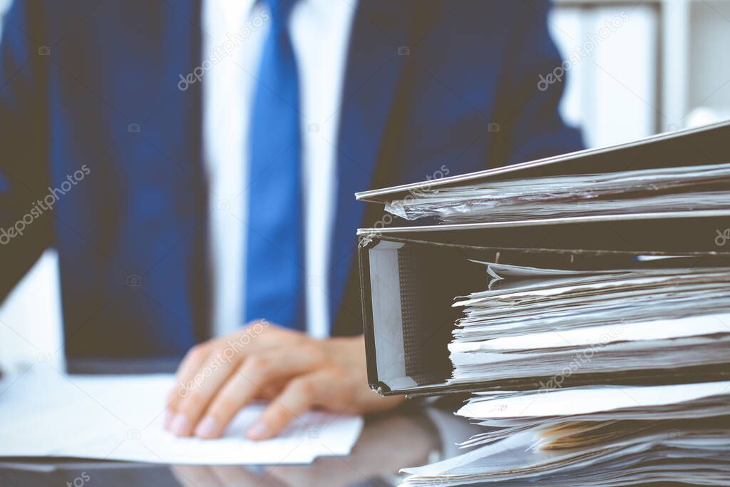 Binders with papers waiting to be processed with businessman or bookkeeper back in blur. Accounting planning budget. Audit, insurance and business concept