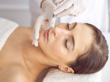 Güzellik uzmanı, genç esmer kadının yüzüne şırıngayla güzellik prosedürü uyguluyor. Kozmetik ilaç ve ameliyat, güzellik iğneleri.