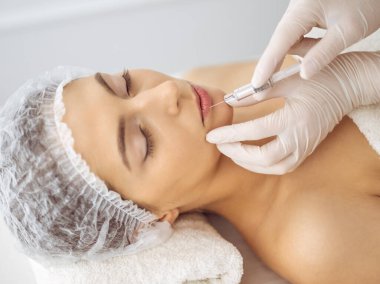 Güzellik uzmanı, genç esmer kadının yüzüne şırıngayla güzellik prosedürü uyguluyor. Kozmetik ilaç ve ameliyat, güzellik iğneleri.