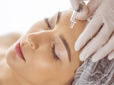 Güzellik uzmanı, genç esmer kadının yüzüne şırıngayla güzellik prosedürü uyguluyor. Kozmetik ilaç ve ameliyat, güzellik iğneleri.