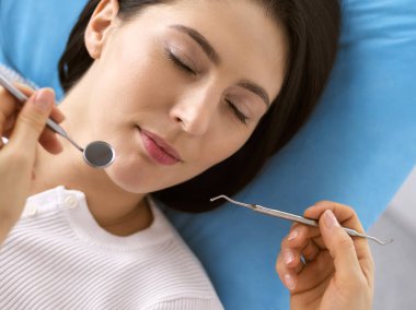 Gülümseyen esmer kadın diş hekimi tarafından muayene ediliyor. Hastanın ağzının yanında diş aletleri tutan bir doktorun elleri. Sağlıklı diş ve ilaç konsepti