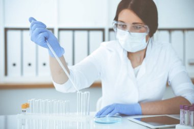 Koruyucu gözlüklü profesyonel kadın bilim adamının laboratuarda reaktörlerle deney yapması. Tıp ve araştırma konsepti