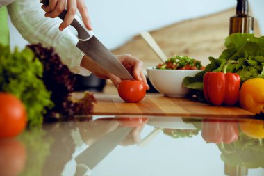Mutfakta pişen bilinmeyen insan elleri. Kırmızı domatesleri dilimleyen kadın. Sağlıklı yemek ve vejetaryen gıda konsepti.