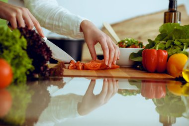 Mutfakta pişen bilinmeyen insan elleri. Kırmızı domatesleri dilimleyen kadın. Sağlıklı yemek ve vejetaryen gıda konsepti.