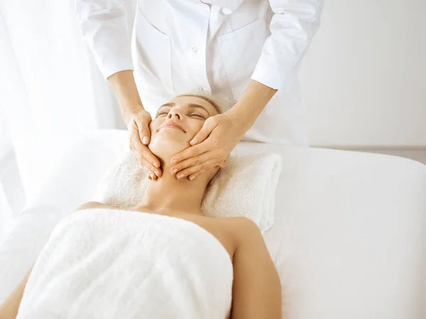 Beautiful blonde woman enjoying facial massage with closed eyes. Relaxing treatment in medicine and spa center concepts