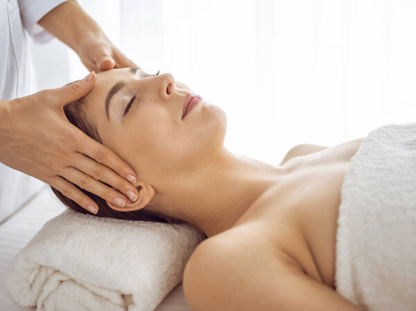 Beautiful brunette woman enjoying facial massage with closed eyes. Relaxing treatment in medicine and spa center concepts