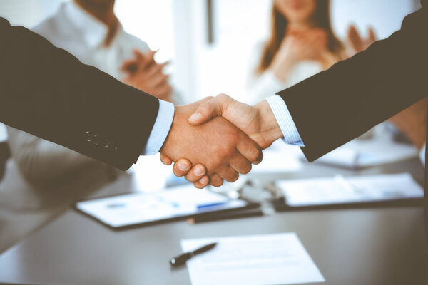 Деловые люди пожимают руки при встрече, в то время как их коллеги хлопают и аплодируют. Группа неизвестных бизнесменов и женщин в современном белом офисе. Командная работа, партнерство и рукопожатие