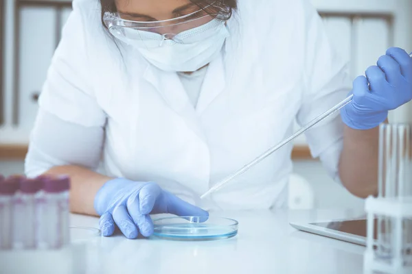 Koruyucu gözlüklü profesyonel kadın bilim adamının laboratuarda reaktörlerle deney yapması. Tıp ve araştırma konsepti