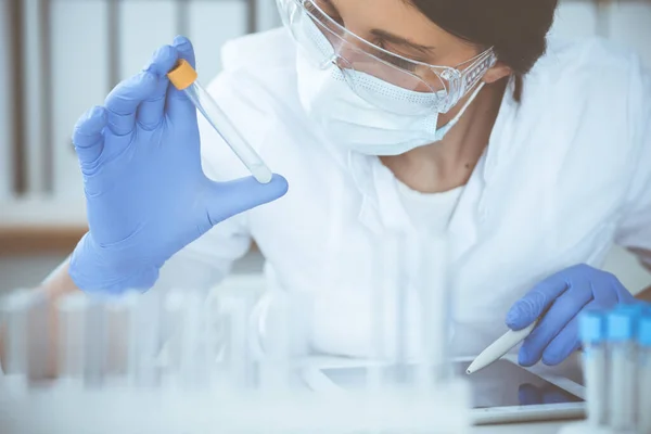 Primer plano de la científica profesional en gafas protectoras haciendo experimento con reactivos en laboratorio. Concepto de medicina e investigación — Foto de Stock