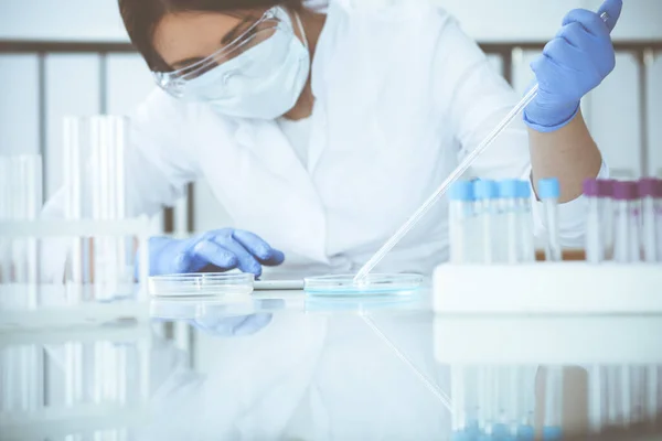 Koruyucu gözlüklü profesyonel kadın bilim adamının laboratuarda reaktörlerle deney yapması. Tıp ve araştırma konsepti