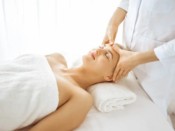 Beautiful blonde woman enjoying facial massage with closed eyes. Relaxing treatment in medicine and spa center concepts Stock Picture