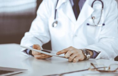 Bilinmeyen erkek doktor klinikteki tablet bilgisayarla yakın planda çalışıyor. İşteki genç doktor. Mükemmel sağlık hizmeti, tıp konsepti