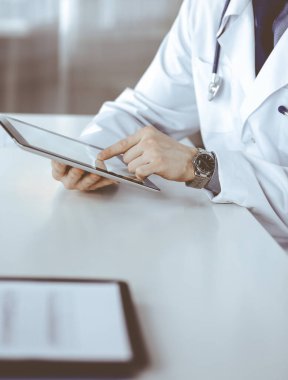 Bilinmeyen erkek doktor klinikteki tablet bilgisayarla yakın planda çalışıyor. İşteki genç doktor. Mükemmel sağlık hizmeti, tıp konsepti