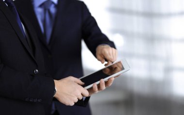 İş adamları yeni projelerini tartışmak için bir tablet bilgisayar kullanıyorlar, modern bir ofiste duruyorlar. İş yerinde iş arkadaşı olan tanınmamış bir iş adamı ya da erkek girişimci. Takım çalışması ve ortaklık