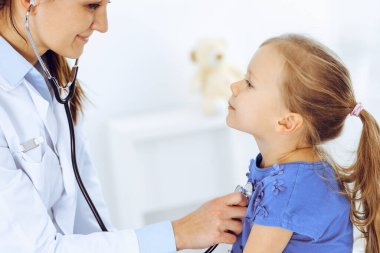 Doktor steteskopla küçük bir kızı muayene ediyor. Her zamanki tıbbi muayenede gülümseyen çocuk hasta. Tıp ve sağlık hizmetleri kavramları