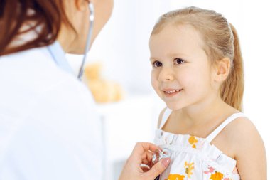 Doktor steteskopla küçük bir kızı muayene ediyor. Her zamanki tıbbi muayenede gülümseyen çocuk hasta. Tıp ve sağlık hizmetleri kavramları