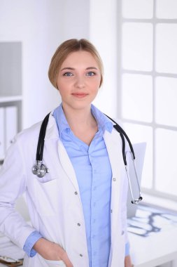 Hastanedeki genç kadın doktor kameraya bakıyor. Mavi renkli terapist bluzu iyi görünüyor. Tıp ve sağlık hizmetleri kavramı