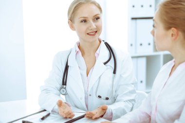 Doktor ve hasta masada otururken hastane ofisinde konuşuyorlar. Tıp alanında sağlık ve müşteri hizmetleri