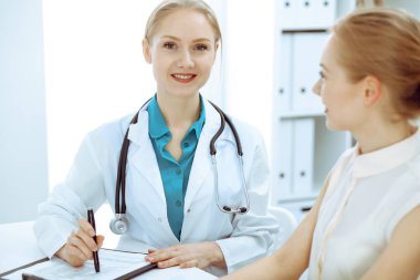 Doktor ve hasta masada otururken hastane ofisinde konuşuyorlar. Tıp alanında sağlık ve müşteri hizmetleri