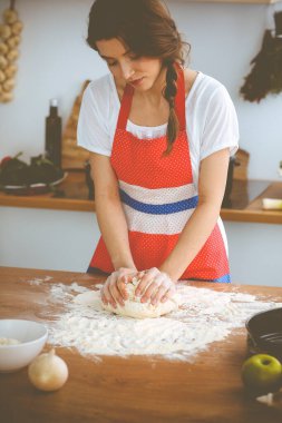 Genç esmer kadın mutfakta pizza ya da el yapımı makarna pişiriyor. Ev hanımı ahşap masada hamur hazırlıyor. Diyet, gıda ve sağlık konsepti