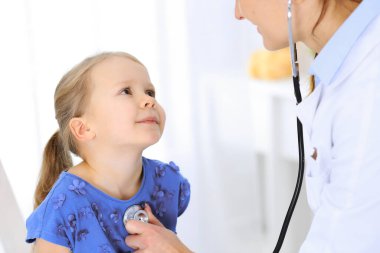 Doktor steteskopla küçük bir kızı muayene ediyor. Her zamanki tıbbi muayenede gülümseyen çocuk hasta. Tıp ve sağlık hizmetleri kavramları