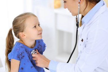 Doktor steteskopla küçük bir kızı muayene ediyor. Her zamanki tıbbi muayenede gülümseyen çocuk hasta. Tıp ve sağlık hizmetleri kavramları