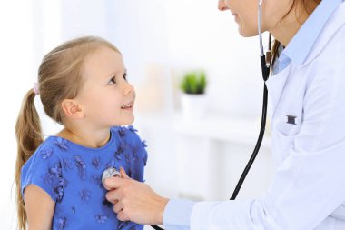 Doktor steteskopla küçük bir kızı muayene ediyor. Her zamanki tıbbi muayenede gülümseyen çocuk hasta. Tıp ve sağlık hizmetleri kavramları