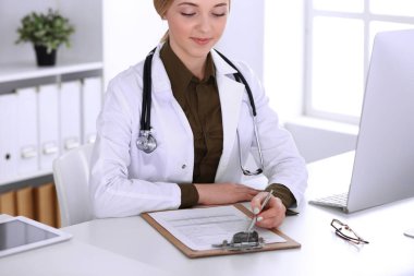 Hastanedeki genç bayan doktor masaüstü bilgisayar monitörüne bakıyor. Doktor ilaç geçmişi ve sınav sonuçlarını kontrol ediyor. Tıp ve sağlık hizmetleri kavramı