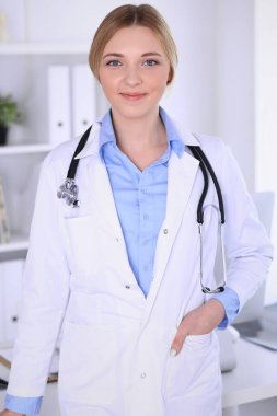 Hastanedeki genç kadın doktor kameraya bakıyor. Mavi renkli terapist bluzu iyi görünüyor. Tıp ve sağlık hizmetleri kavramı