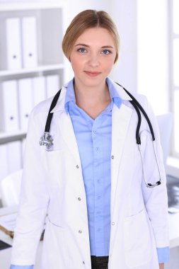 Hastanedeki genç kadın doktor kameraya bakıyor. Mavi renkli terapist bluzu iyi görünüyor. Tıp ve sağlık hizmetleri kavramı