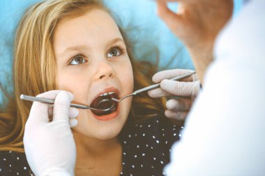 Doktor muayenesi sırasında ağzı açık bir şekilde dişçi koltuğunda oturan küçük kız. Dişçi muayenehanesi. Tıp konsepti. Renkli fotoğraf