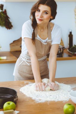 Genç esmer kadın mutfakta pizza ya da el yapımı makarna pişiriyor. Ev hanımı ahşap masada hamur hazırlıyor. Diyet, gıda ve sağlık konsepti