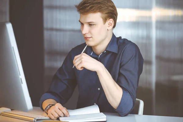 Jeune homme d'affaires blond réfléchissant à la stratégie à son lieu de travail avec ordinateur. Démarrage d'entreprise signifie travailler dur et hors du temps pour la réussite — Photo