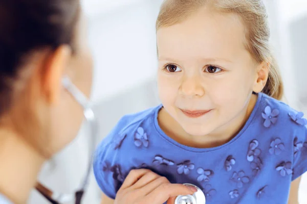 Arzt untersucht ein kleines Mädchen per Stethoskop. Glücklich lächelnder Kinderpatient bei der üblichen ärztlichen Untersuchung. Medizin- und Gesundheitskonzepte — Stockfoto