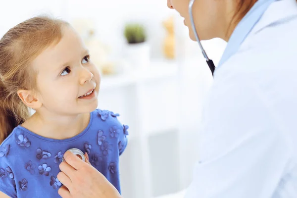 닥터가 청진기로 어린 소녀를 진찰하고 있어. 평상시의 진료 에서 미소짓는 어린이 환자에게 행복 한 미소를 짓는다. 의학 과 의료 개념 — 스톡 사진