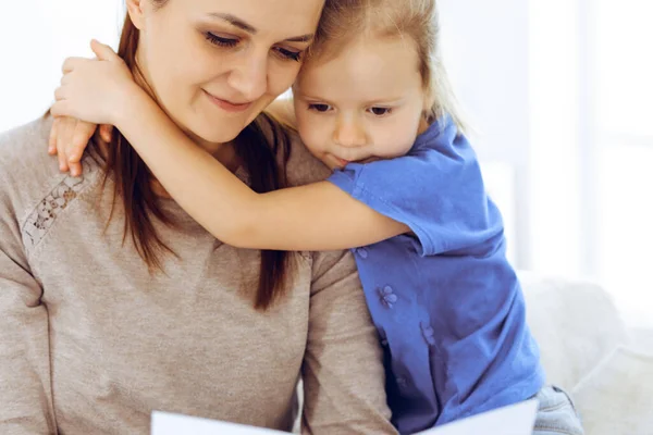 Muttertagskonzept. Die Tochter gratuliert der Mutter und überreicht ihr eine Postkarte mit rotem Herzchen. Mutter und Mädchen glücklich lächelnd und umarmt. Familienspaß und Urlaub — Stockfoto