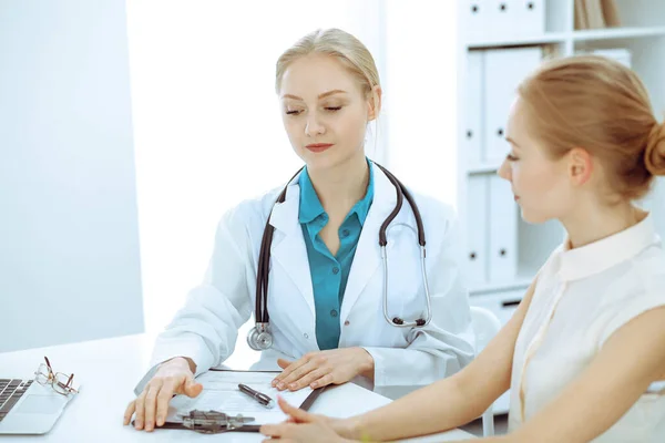 Dottore e paziente che parlano nello studio dell'ospedale mentre sono seduti alla scrivania. Assistenza sanitaria e servizio clienti in medicina — Foto Stock