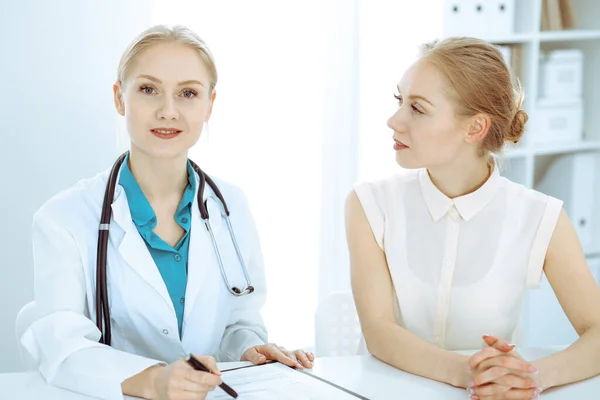 Doktor a pacient si povídají v nemocniční kanceláři, zatímco sedí za stolem. Zdravotní péče a klientské služby v medicíně — Stock fotografie
