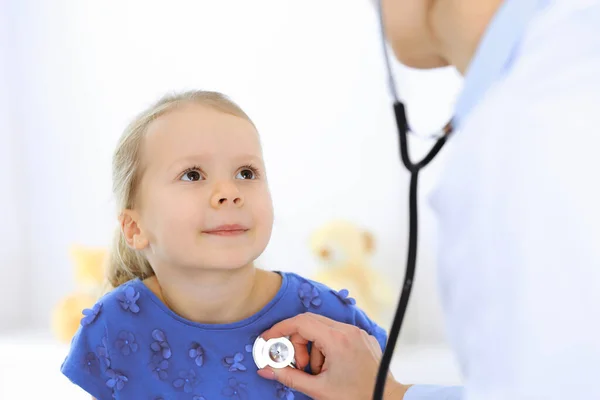 Arzt untersucht ein kleines Mädchen per Stethoskop. Glücklich lächelnder Kinderpatient bei der üblichen ärztlichen Untersuchung. Medizin- und Gesundheitskonzepte — Stockfoto