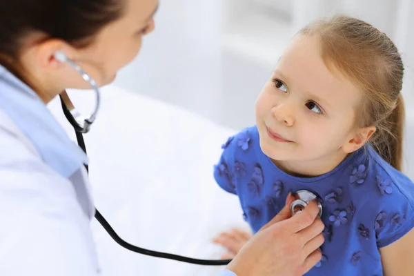 Arzt untersucht ein kleines Mädchen per Stethoskop. Glücklich lächelnder Kinderpatient bei der üblichen ärztlichen Untersuchung. Medizin- und Gesundheitskonzepte — Stockfoto