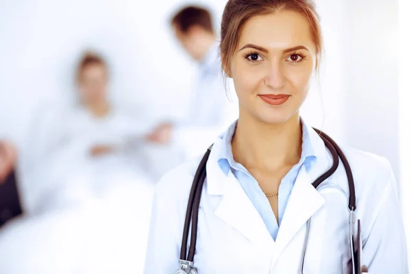 Doctora sonriendo en el fondo con paciente en la cama y dos doctores — Foto de Stock