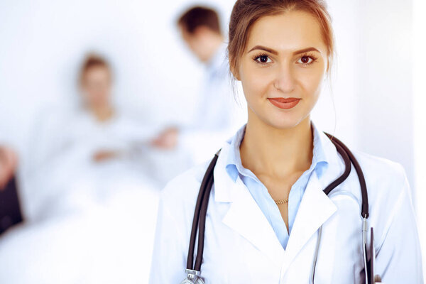 Female doctor smiling on the background with patient in the bed and two doctors