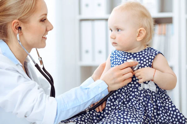 Médico y paciente en el hospital. Niña vestida con vestido azul oscuro en guisantes está siendo examinada por el médico con estetoscopio. Concepto de medicina — Foto de Stock