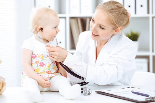 Arzt und Patient Kleinkind im Krankenhaus. Kleines Mädchen im Kleid mit rosa Blüten wird vom Arzt mit Stethoskop untersucht. Medizinkonzept — Stockfoto