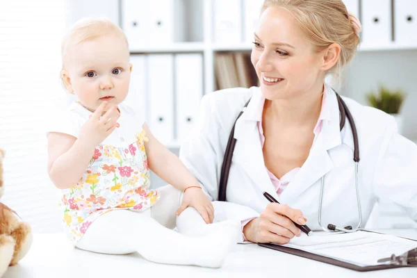 Doctor and patient toddler in hospital. Little girl dressed in dress with pink flowers is being examined by doctor with stethoscope. Medicine concept