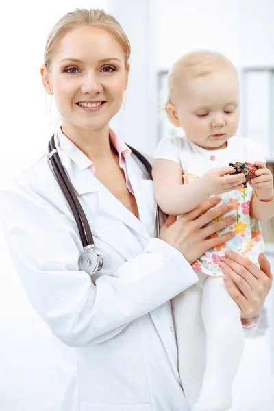 Doctor and patient toddler in hospital. Little girl dressed in dress with pink flowers is being examined by doctor with stethoscope. Medicine concept