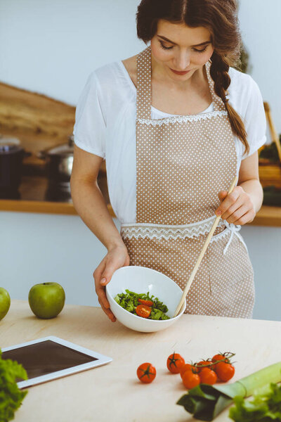Молодая брюнетка готовит на кухне. Домохозяйка держит в руке деревянную ложку. Концепция питания и здоровья
