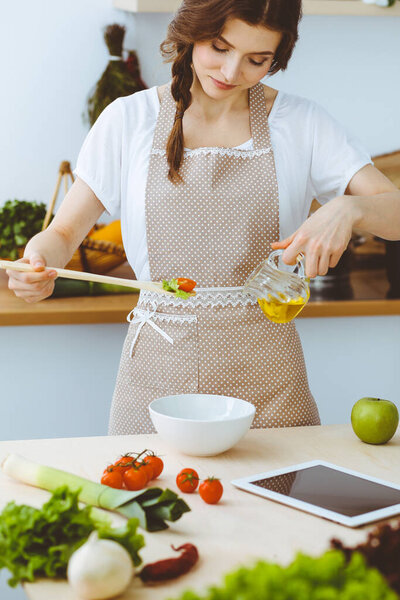 Молодая брюнетка готовит на кухне. Домохозяйка держит в руке деревянную ложку. Концепция питания и здоровья